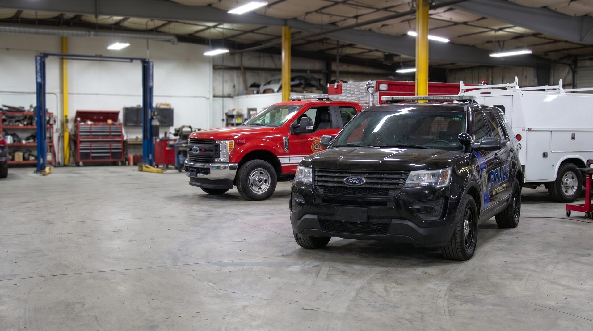 A police interceptor, fire-department truck, and commercial work van being repaired inside TriState Collision Center